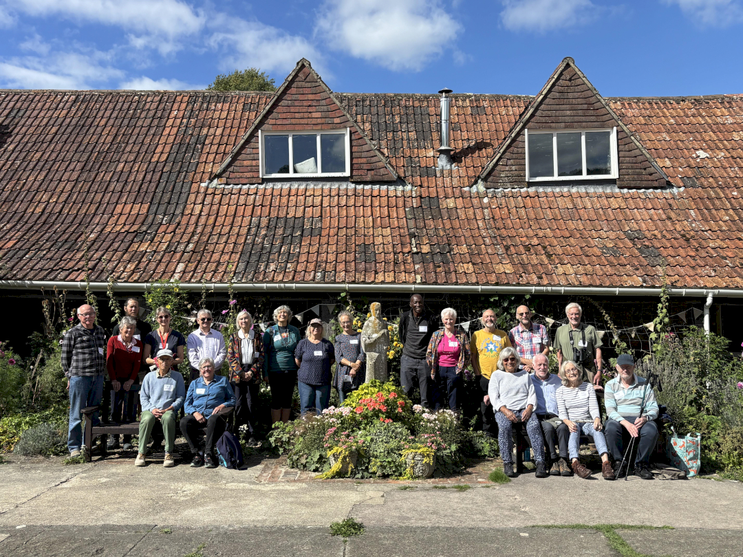 standing group smiling at the camera in sunshine in front of a large roof